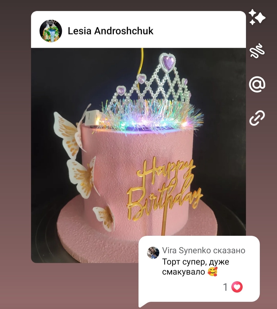 Różowy tort urodzinowy zdobiony złotym napisem, motylami i koroną z lampek LED, umieszczony na różowej podstawie. Widoczne komentarze użytkowników.