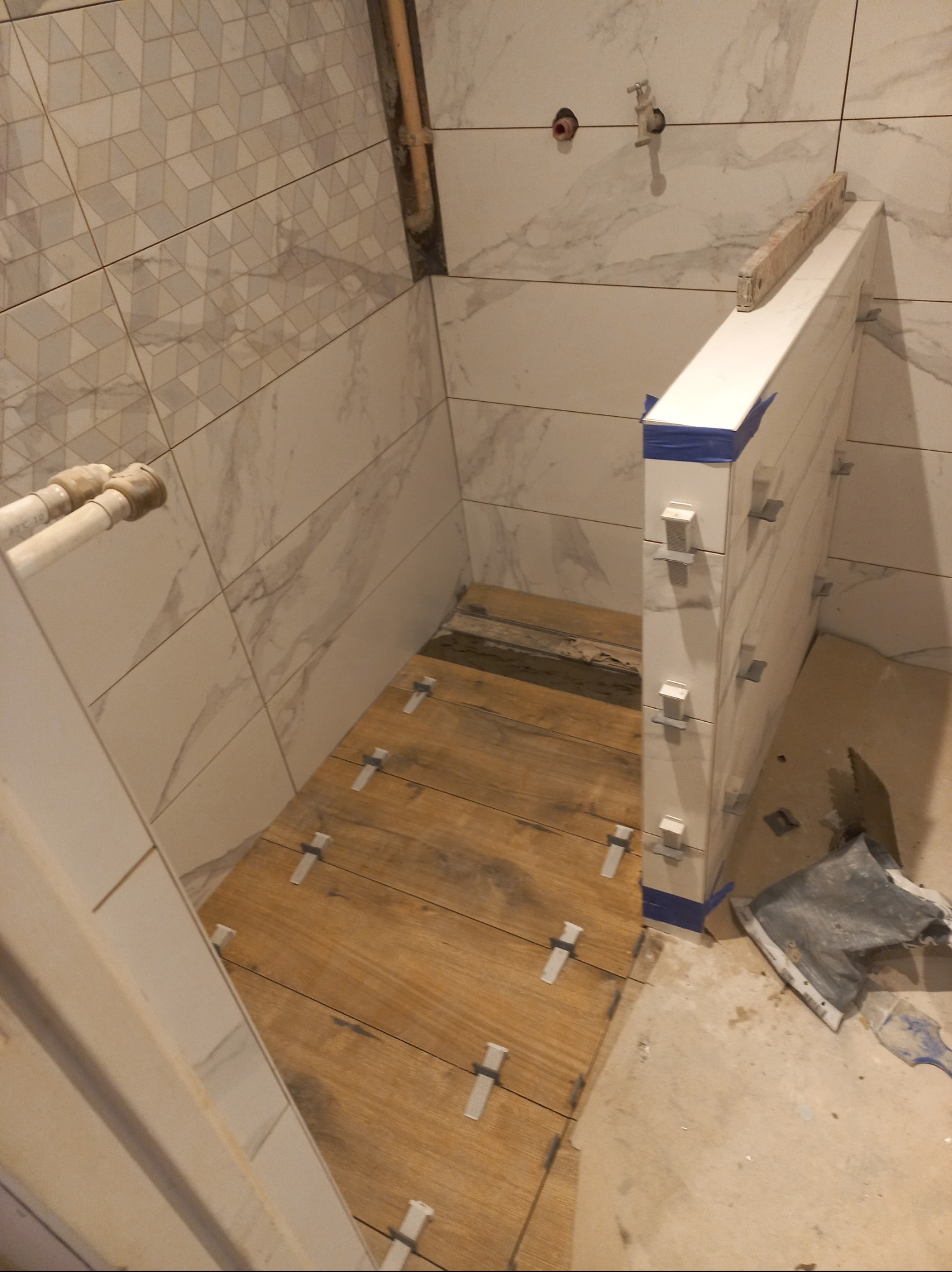 Wnętrze łazienki w trakcie prac wykończeniowych. Widoczne płytki na ścianach i podłodze, elementy instalacji oraz narzędzia glazurnicze.