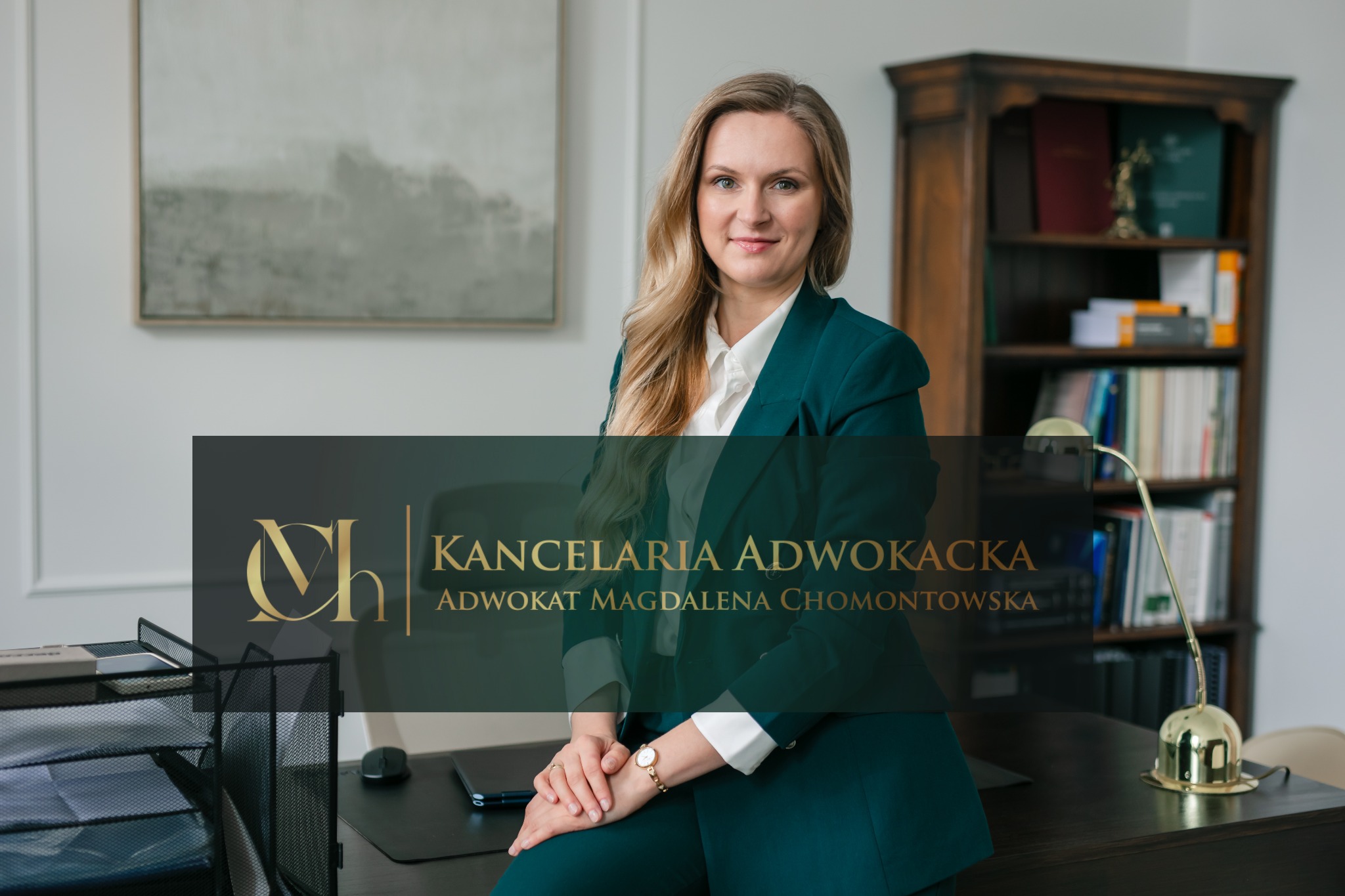 Portret uśmiechniętej adwokatki Magdaleny Chomontowskiej w zielonym garniturze, siedzącej na biurku w kancelarii, z regałem na książki w tle.