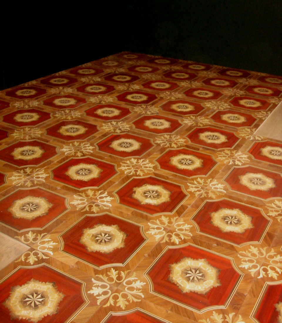 Dekoracyjna podłoga parkietowa z czerwonymi, ośmiokątnymi wstawkami i kremowymi rozetami, ułożona we wzór na ciemnym tle.