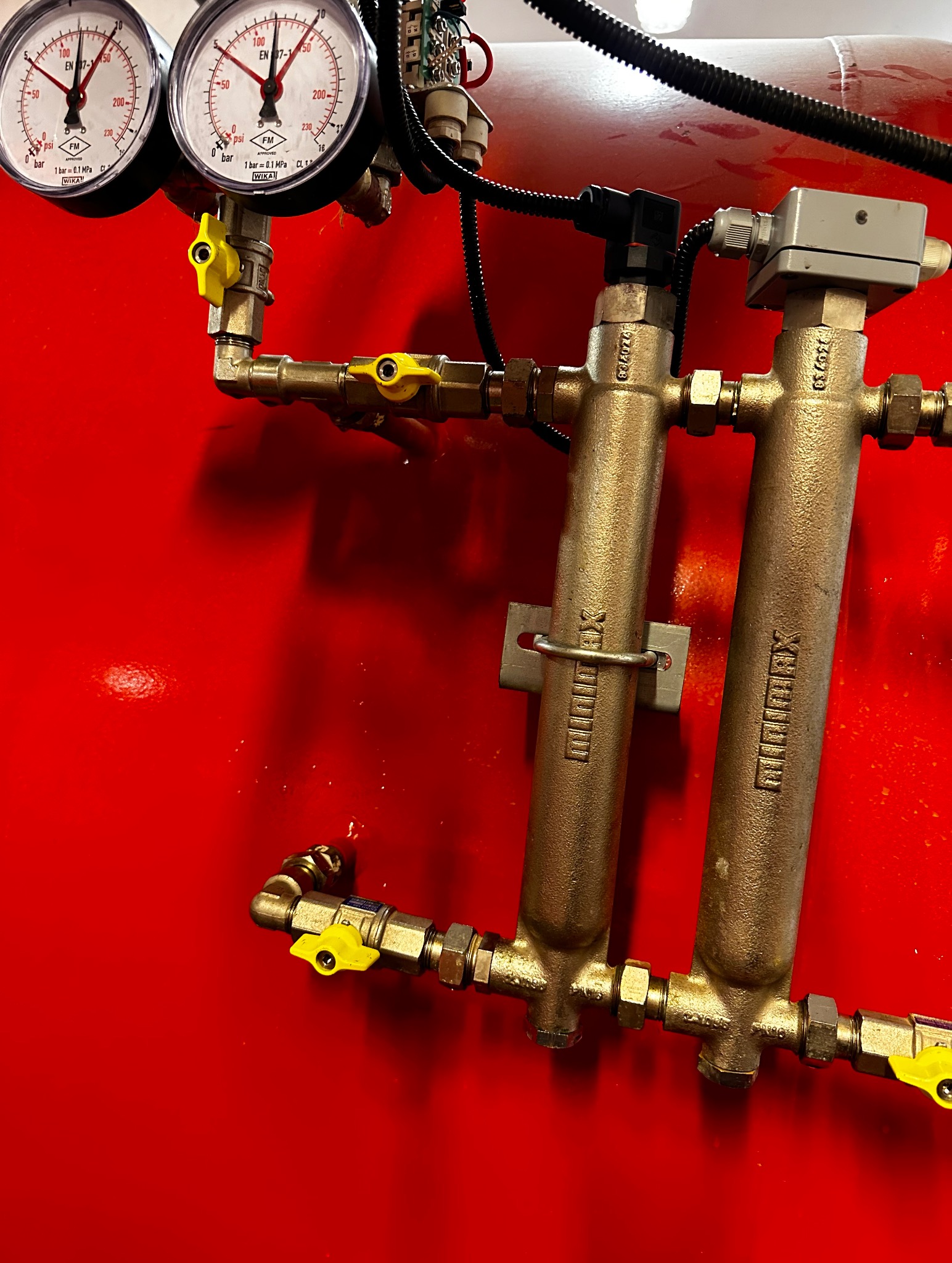Czerwony zbiornik z manometrami i instalacją hydrauliczną z żółtymi zaworami. Widoczne filtry z oznaczeniem Reflex.