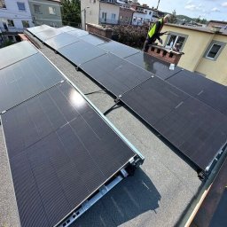 Doktor Klimat Pompy Ciepła - Panele fotowoltaiczne na dachu budynku mieszkalnego, montowane przez instalatora w odblaskowej kamizelce, w słoneczny dzień. Widok z góry.