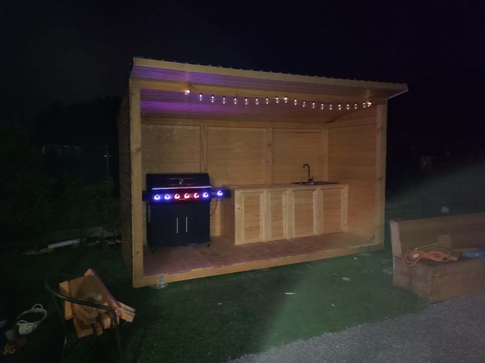 Drewniana altana z grillem i blatem roboczym, oświetlona girlandą, wykonana w Goleniowie. Nowoczesny design.