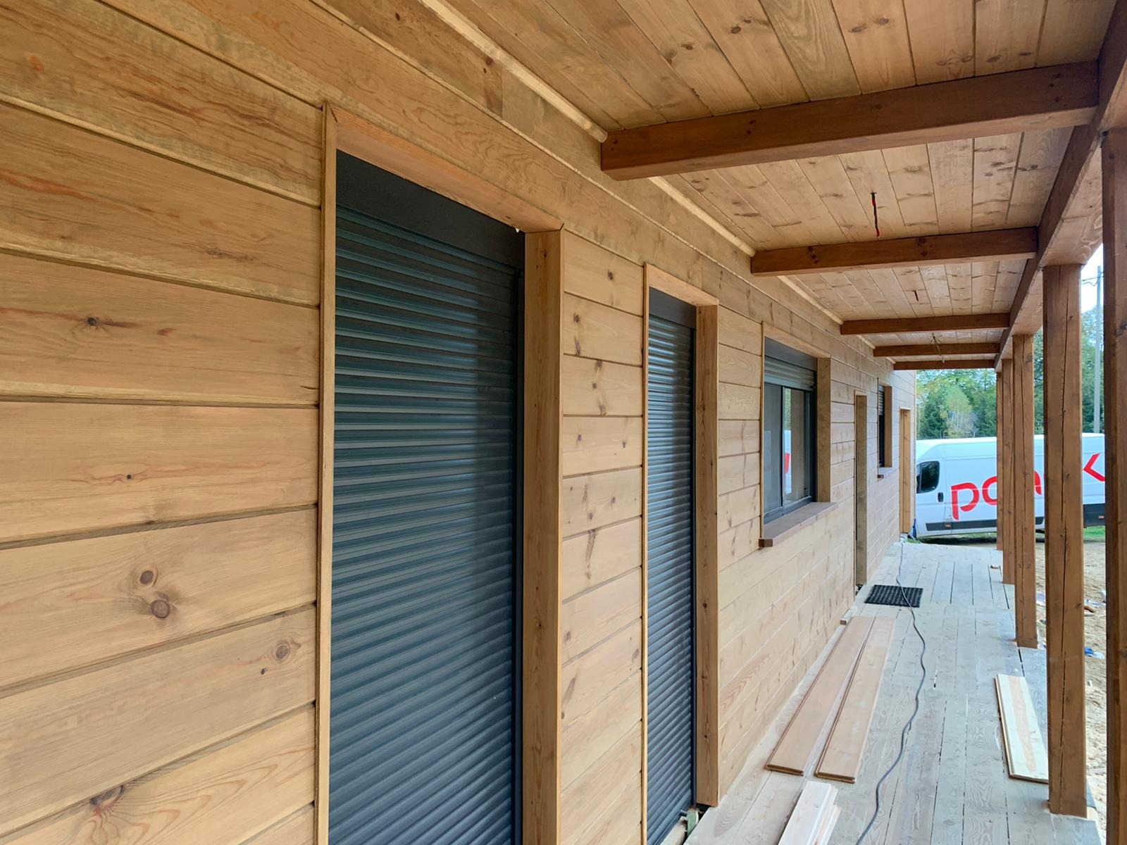 Drewniana elewacja budynku z zamontowanymi, opuszczonymi roletami zewnętrznymi w kolorze grafitowym. Widok z zewnątrz, z boku budynku.