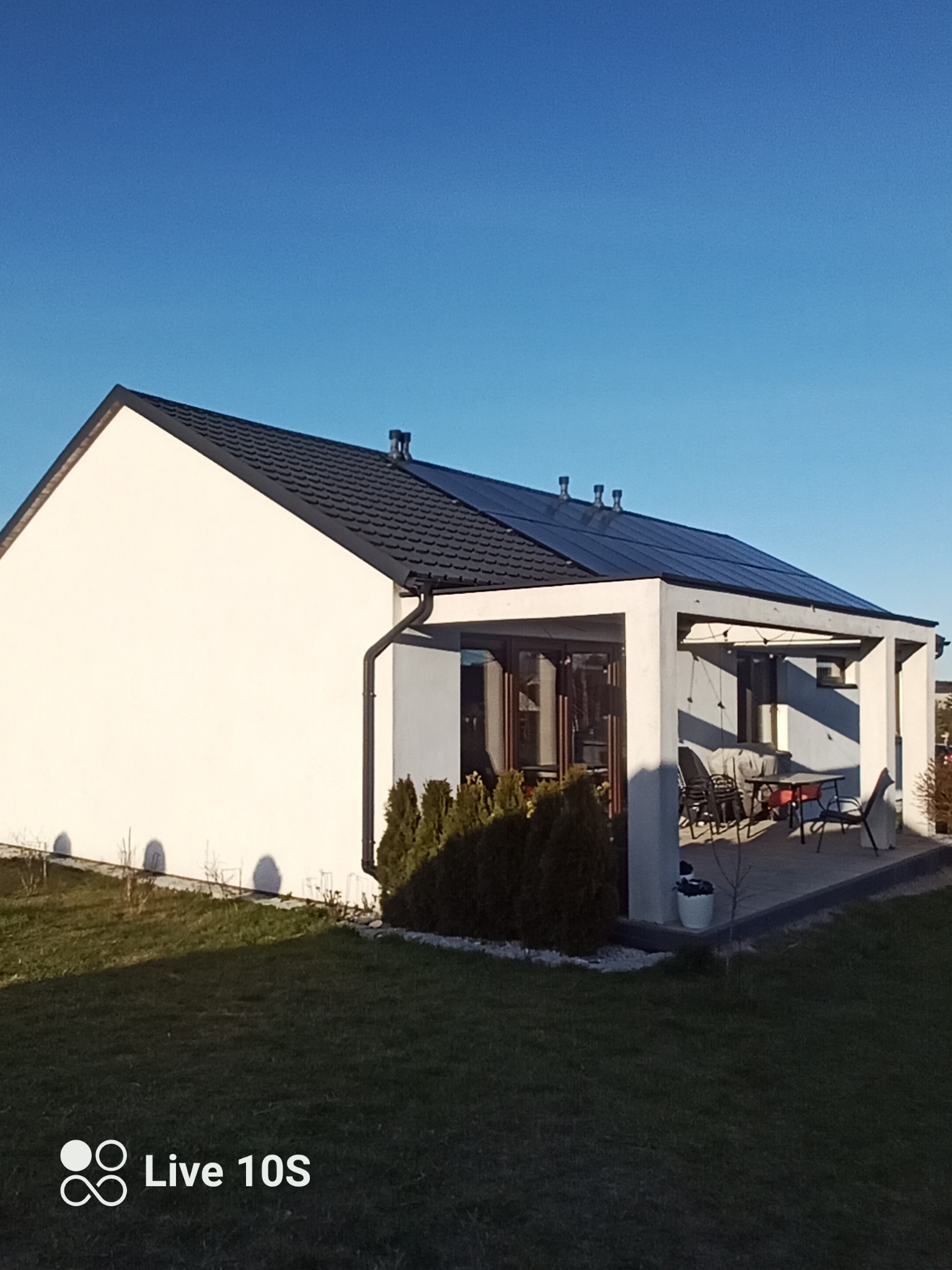 Dom jednorodzinny z ciemnym dachem i rynnami, widok z boku na tle błękitnego nieba. Na dachu widoczne kominki wentylacyjne.