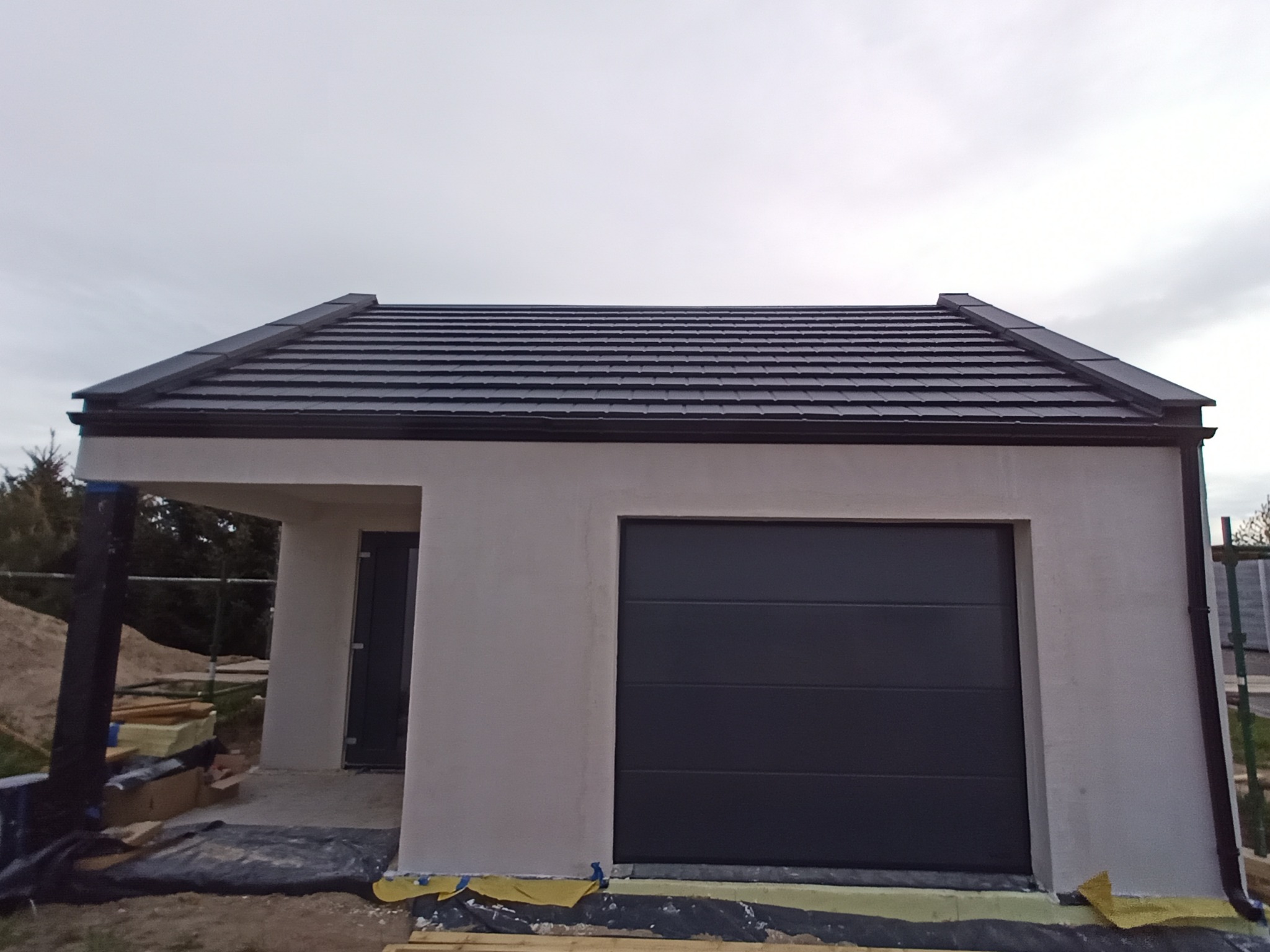 Nowoczesny garaż z ciemną, płaską dachówką i rynnami. Widoczne detale wykończenia dachu i elewacji. Ujęcie z dołu, podkreślające geometrię konstrukcji.