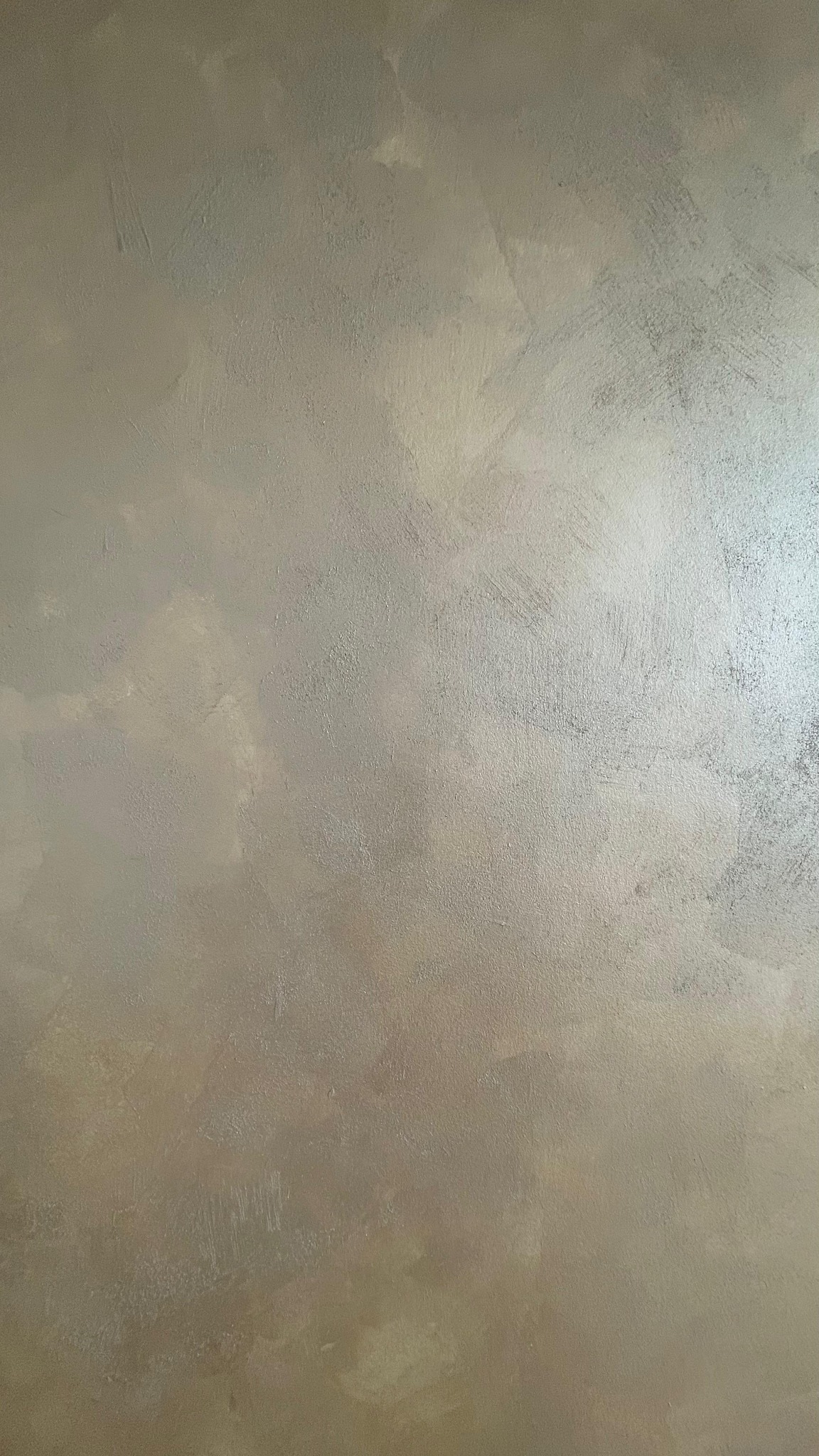 Beżowa ściana z fakturą, imitująca naturalny kamień, z delikatnym połyskiem. Widoczne ślady pędzla i nieregularne wzory. Oświetlenie z prawej strony podkreśla strukturę.