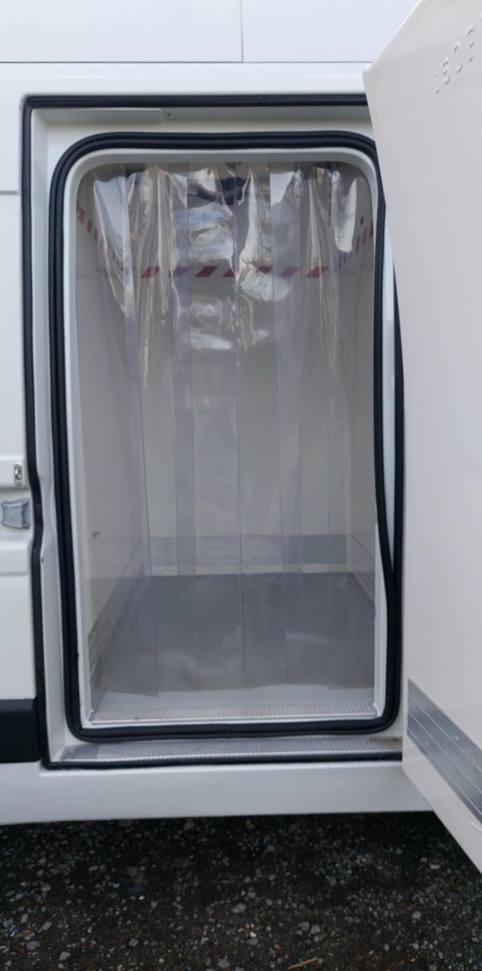 Otwarta tylna przestrzeń ładunkowa białego samochodu dostawczego z kurtyną paskową z tworzywa sztucznego, widok na pusta przestrzeń ładunkową.