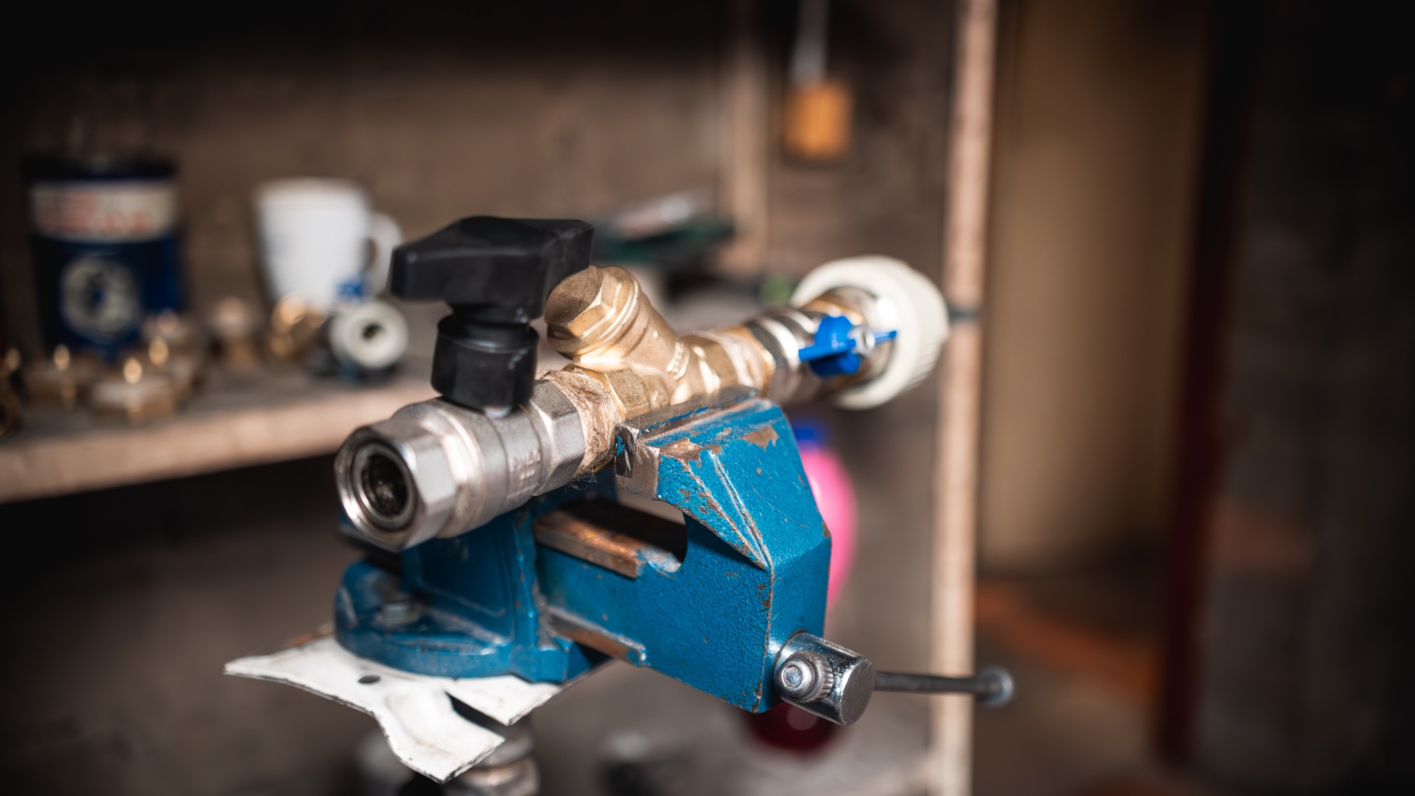 Zacisk śrubowy trzyma złączki instalacyjne z mosiądzu i metalu. Na półce widoczne akcesoria instalacyjne. Warsztatowe ujęcie.