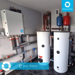 JR7 FINANZAS Robert Jędrzejczyk - Złożona instalacja grzewcza z dwoma białymi zbiornikami w Częstochowie. Szare rury z izolacją, czerwone i niebieskie elementy. Nowoczesny system w kotłowni.