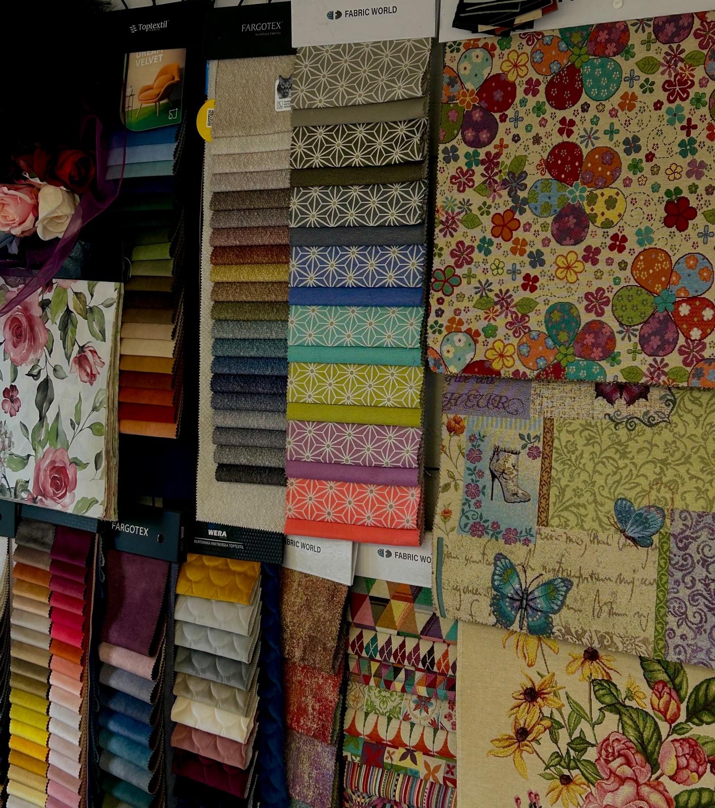 Ekspozycja próbek tkanin obiciowych z różnorodnymi wzorami i fakturami, w tym kwiatowe motywy i geometryczne desenie. Paleta kolorów od stonowanych po intensywne.