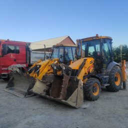 SDB Zenon Młynek - Ciężarówki i koparko-ładowarki JCB na placu budowy, z widocznym żwirem w tle, sugerujące prace ziemne i transport materiałów budowlanych.