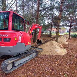 SDB Zenon Młynek - Czerwona mini koparka Volvo ECR35D w lesie, wykonuje wykop. W tle widoczny pryzmat ziemi.