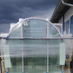 MAK Consulting p.h.u. Michał Nowak - Zapakowane okna PCV z czarnymi ramami i oknem w kształcie łuku na górze, przygotowane do transportu na tle pochmurnego nieba.