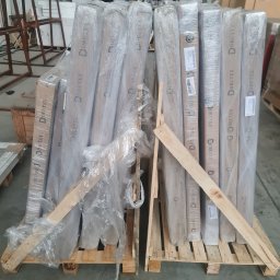 MAK Consulting p.h.u. Michał Nowak - Paleta z zapakowanymi w folię elementami stolarki, prawdopodobnie drzwiami, z widocznym logo Drutex, zabezpieczona drewnianymi listwami, w magazynie.