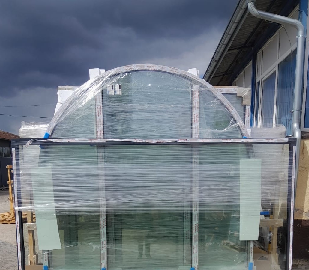 Zapakowane okna PCV z czarnymi ramami i oknem w kształcie łuku na górze, przygotowane do transportu na tle pochmurnego nieba.