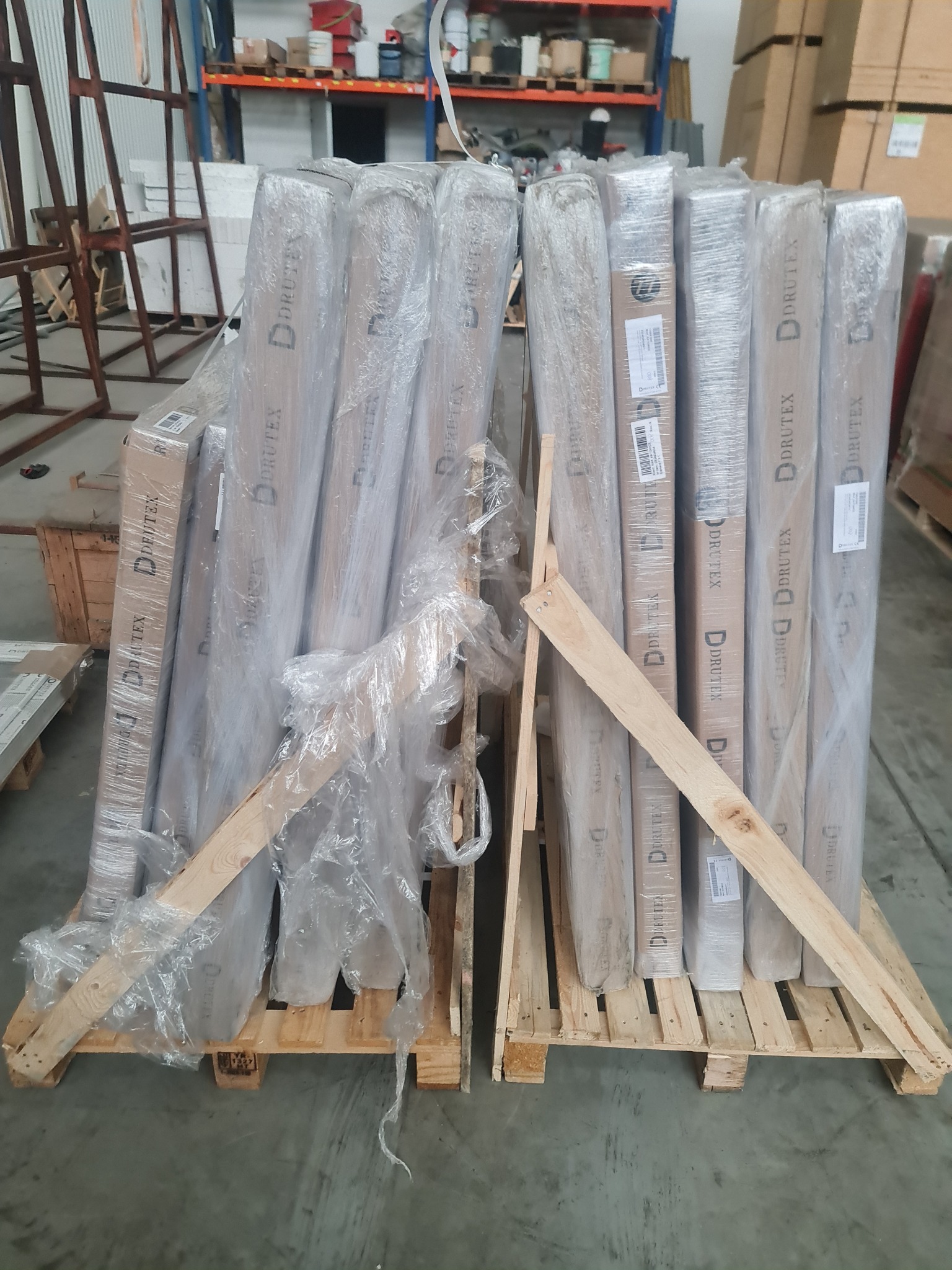 Paleta z zapakowanymi w folię elementami stolarki, prawdopodobnie drzwiami, z widocznym logo Drutex, zabezpieczona drewnianymi listwami, w magazynie.