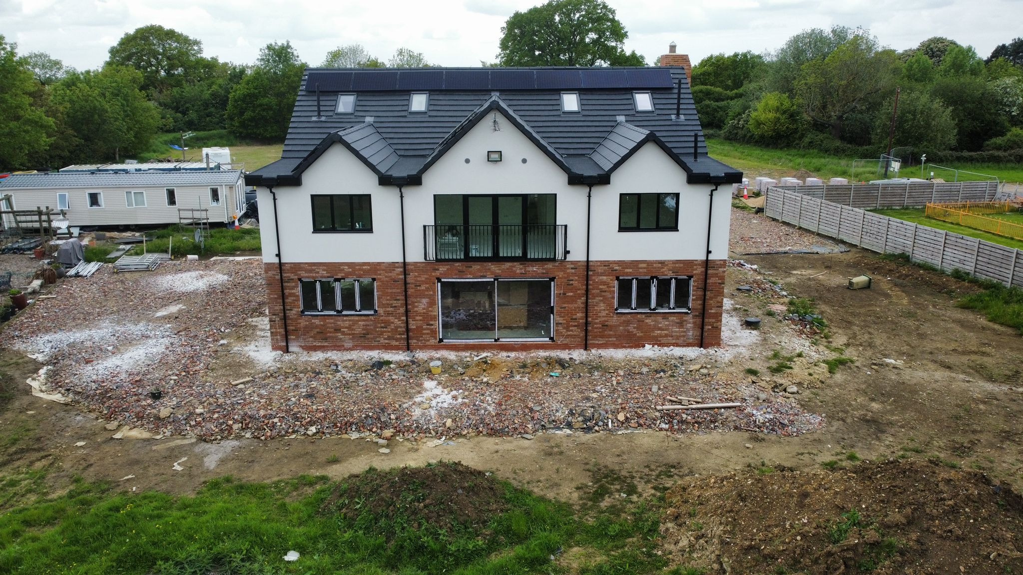 Nowoczesny dom z czarnymi oknami i drzwiami balkonowymi, wykończony cegłą i białym tynkiem, z panelami słonecznymi na dachu, widziany z lotu ptaka.