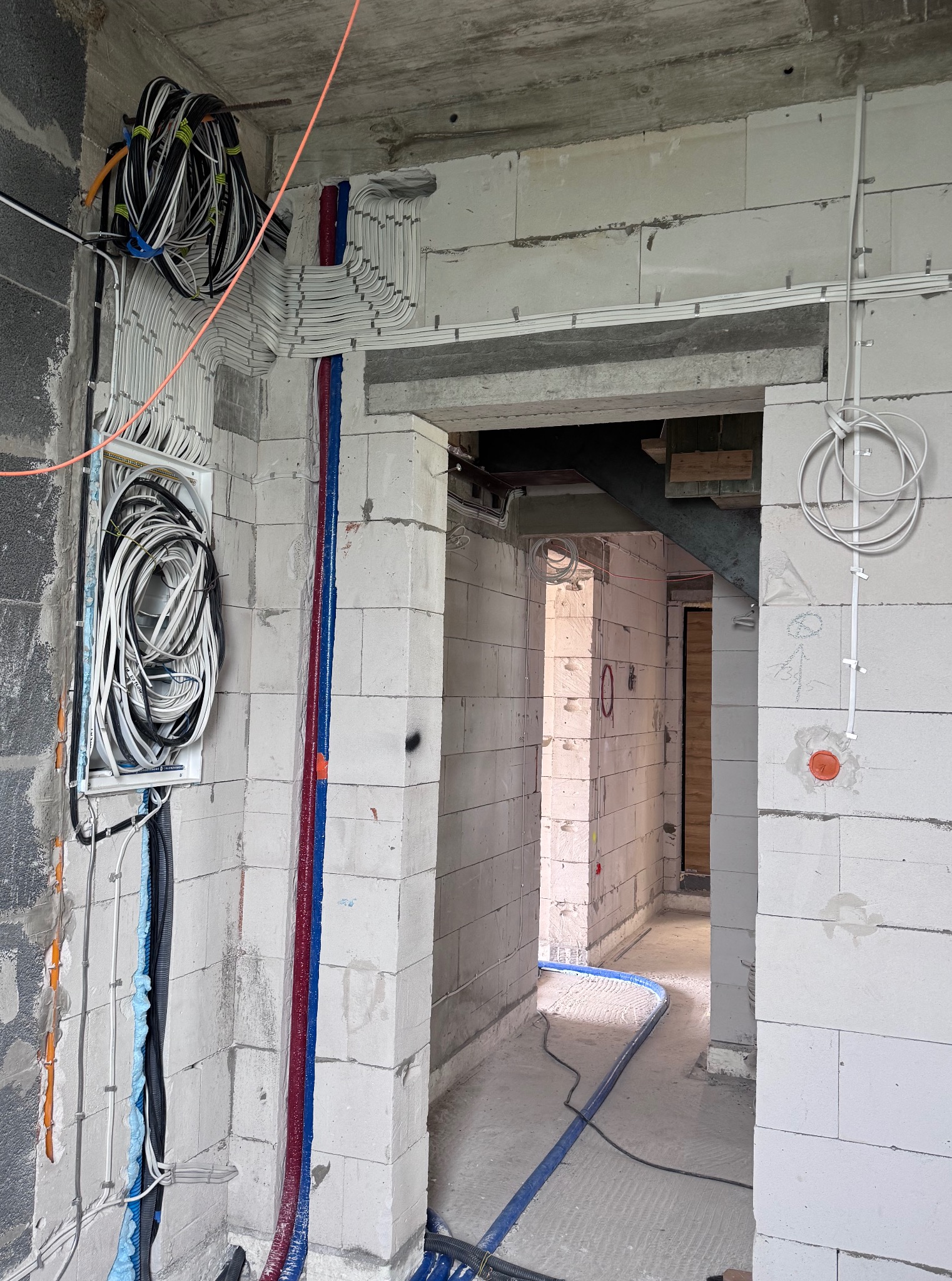 Nierówne ściany z betonu komórkowego w trakcie prac. Widoczne kable w peszlach i skrzynka z kablami. Część kabli ułożona w korytach. Surowy stan.