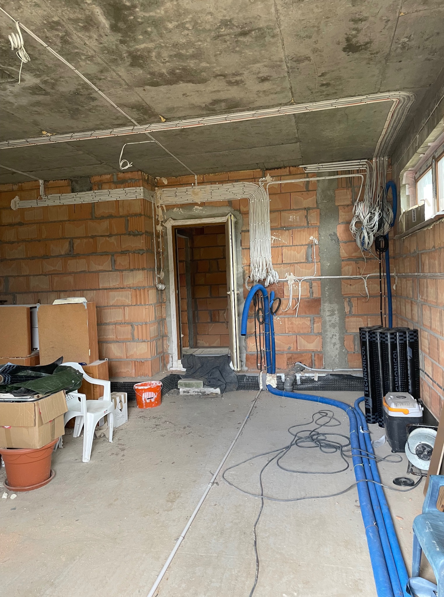 Surowy stan: instalacja elektryczna w budynku z czerwonej cegły. Widoczne kable i rury prowadzone po ścianach i suficie, przygotowane do dalszych prac wykończeniowych.