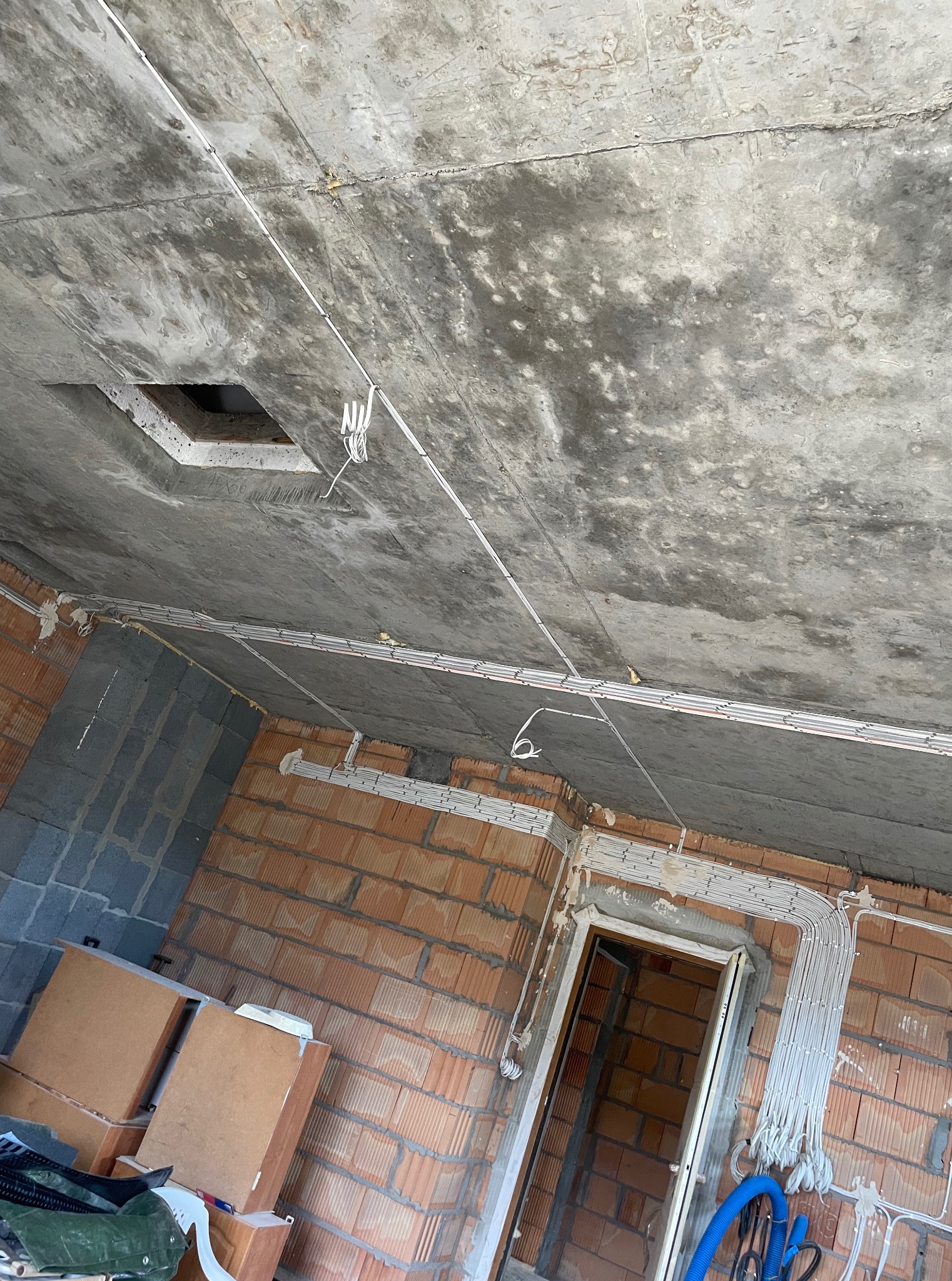 Surowy strop z widocznymi kablami elektrycznymi w peszlach, ułożonymi wzdłuż ścian z czerwonej cegły. Otwór wentylacyjny w suficie. Instalacja w trakcie realizacji.