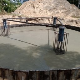 WAMKO Mateusz Kowalczyk - Zalany fundament okrągły z metalowym szalunkiem i zbrojeniem, widok z góry. W tle ziemia i drzewa.