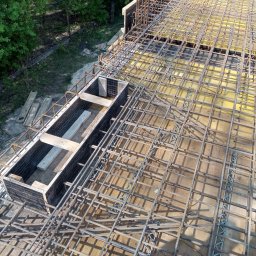 WAMKO Mateusz Kowalczyk - Zbrojenie stropu z widoczną szalunkową formą, przygotowane do zalania betonem. Widok z góry ukazuje siatkę prętów i drewniane elementy konstrukcji.