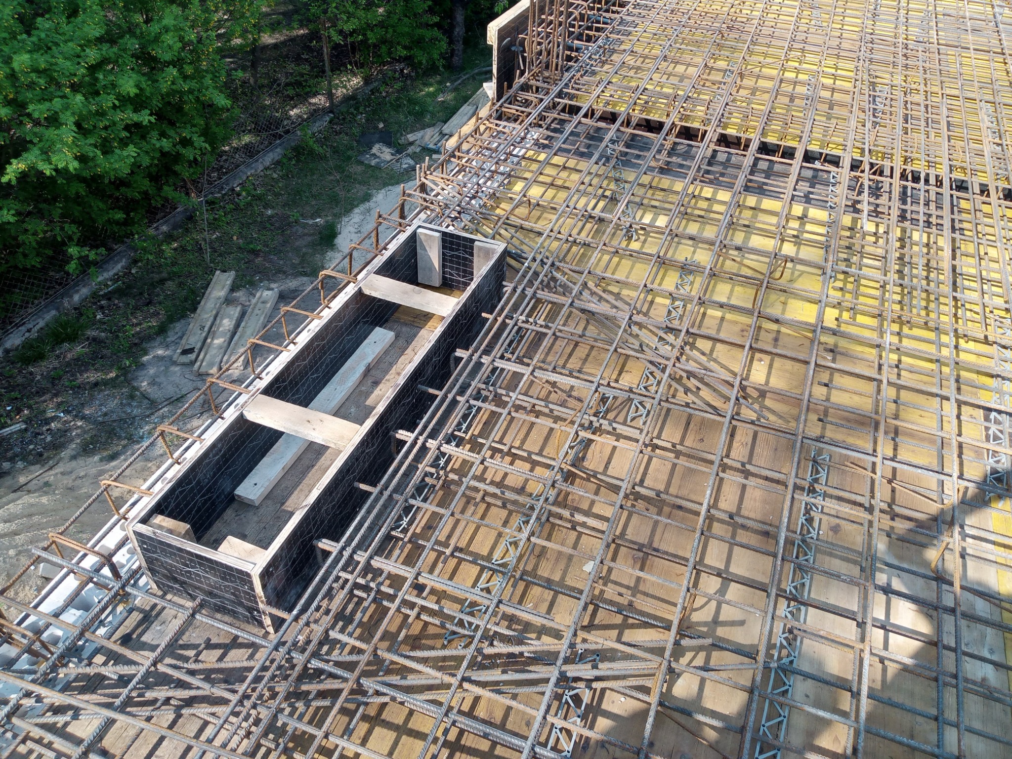Zbrojenie stropu z widoczną szalunkową formą, przygotowane do zalania betonem. Widok z góry ukazuje siatkę prętów i drewniane elementy konstrukcji.