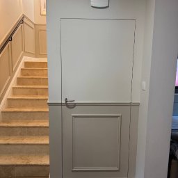 Renovest - Wykończenie Wnętrz - Ukryte drzwi w panelowej ścianie, dopasowane kolorystycznie do schodów z trawertynu i parkietu w jodełkę. Minimalistyczny design, listwy przypodłogowe.
