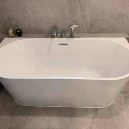 Renovest - Wykończenie Wnętrz - Nowoczesna, wolnostojąca wanna w łazience wykończonej szarym marmurem. Minimalistyczna armatura i dekoracje na półce dodają elegancji. Ujęcie z góry.