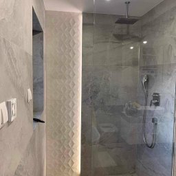 Renovest - Wykończenie Wnętrz - Nowoczesna łazienka z kabiną prysznicową typu walk-in, szare płytki imitujące marmur i dekoracyjna ściana z podświetlonymi, trójwymiarowymi panelami.