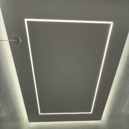 Renovest - Wykończenie Wnętrz - Nowoczesna łazienka z podświetlanym sufitem w kształcie kwadratu. Białe płytki na ścianach. Czarna deszczownica. Minimalistyczny design z efektem subtelnego oświetlenia.