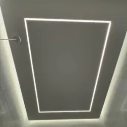 Nowoczesna łazienka z podświetlanym sufitem w kształcie kwadratu. Białe płytki na ścianach. Czarna deszczownica. Minimalistyczny design z efektem subtelnego oświetlenia.