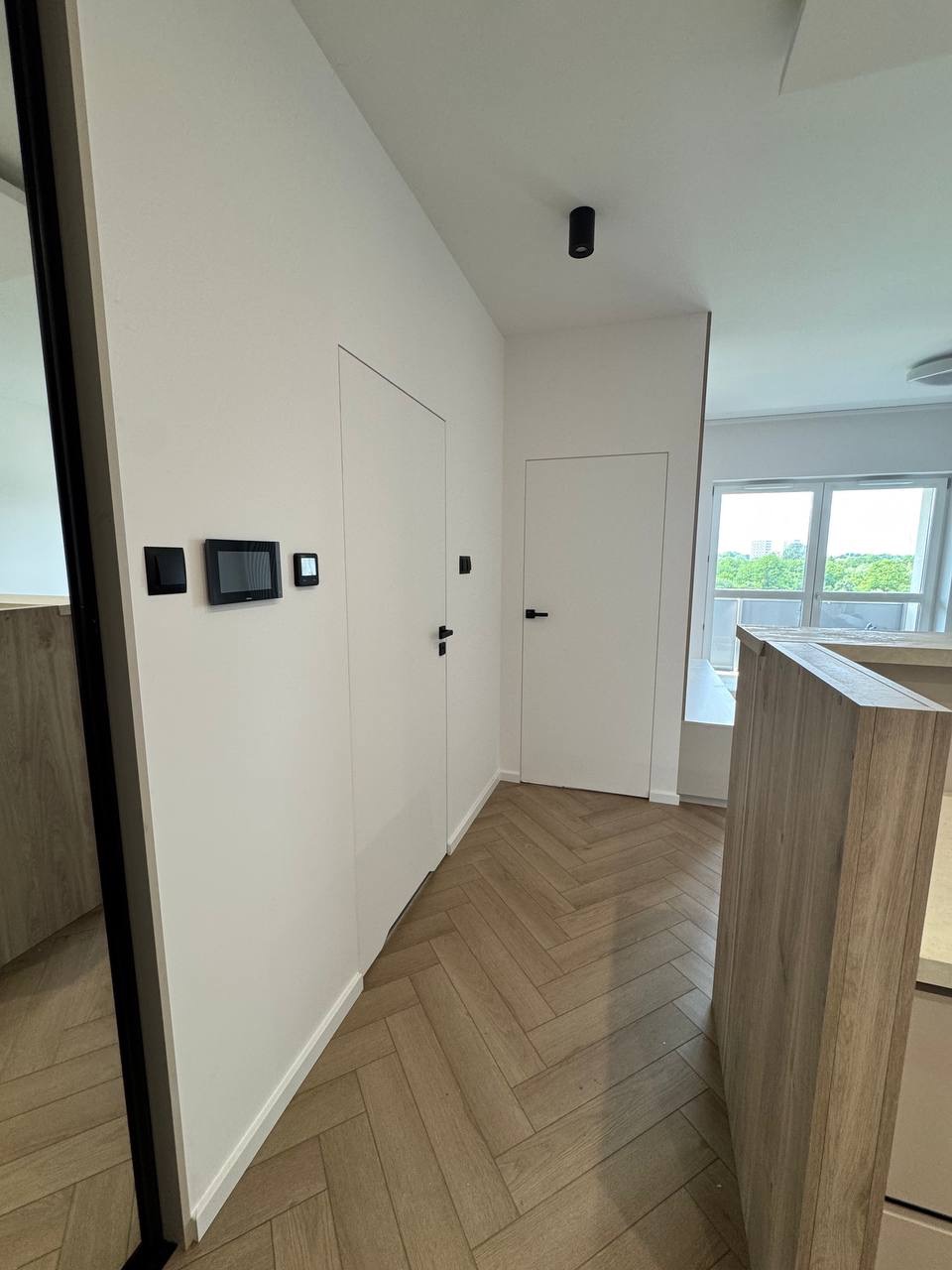 Nowoczesny przedpokój z ukrytymi drzwiami i parkietem w jodełkę. Minimalistyczny design, białe ściany, czarne akcenty oświetleniowe i sterowanie inteligentnym domem.
