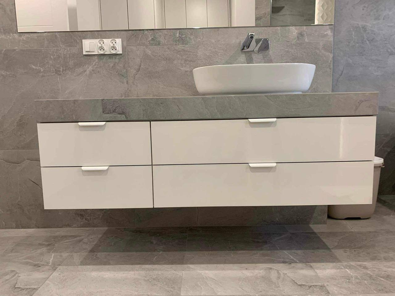 Nowoczesna łazienka: biała szafka pod umywalką z szufladami i blatem z szarego kamienia, okrągła umywalka nablatowa, szare płytki na ścianie i podłodze.