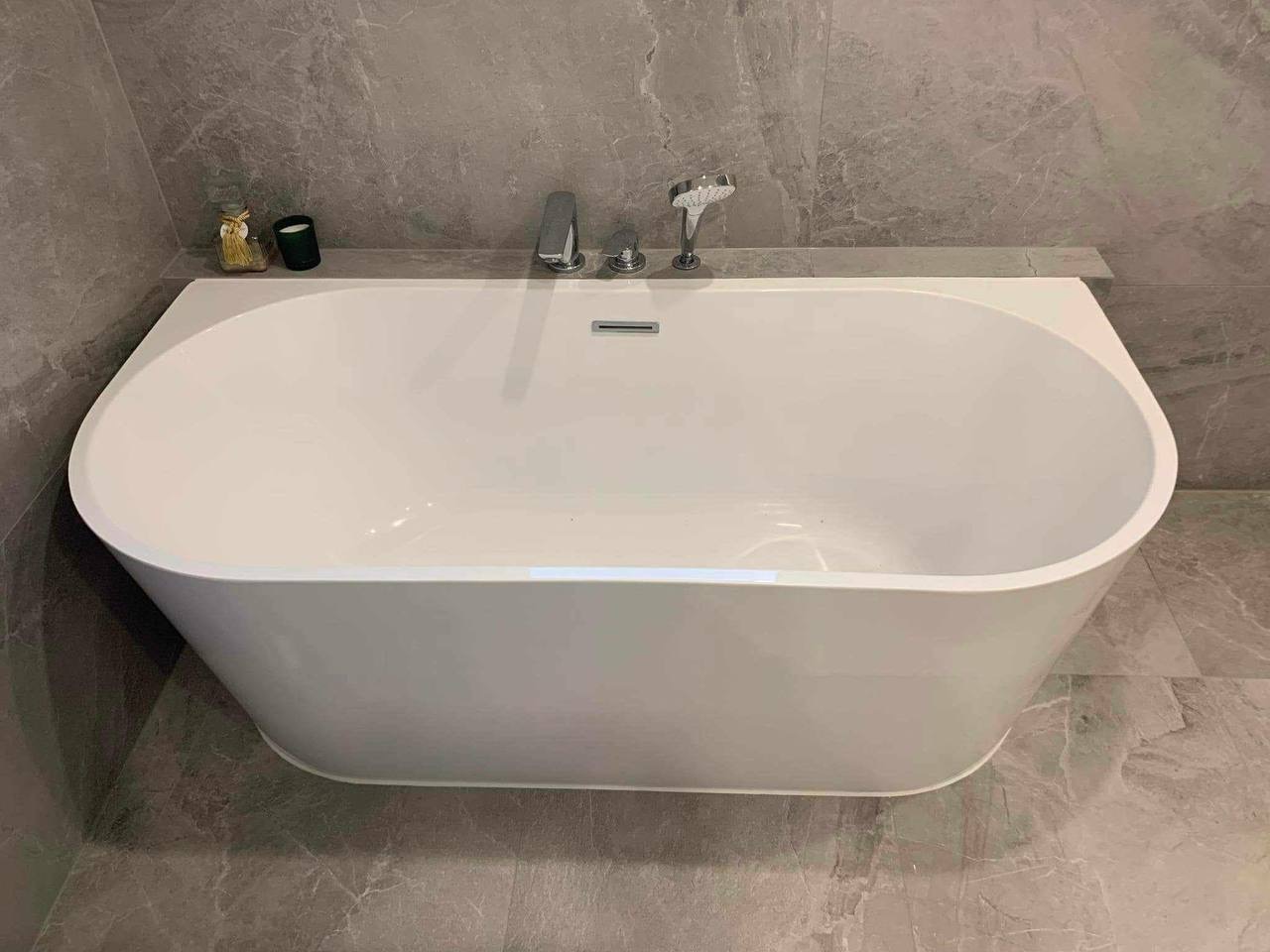 Nowoczesna, wolnostojąca wanna w łazience wykończonej szarym marmurem. Minimalistyczna armatura i dekoracje na półce dodają elegancji. Ujęcie z góry.