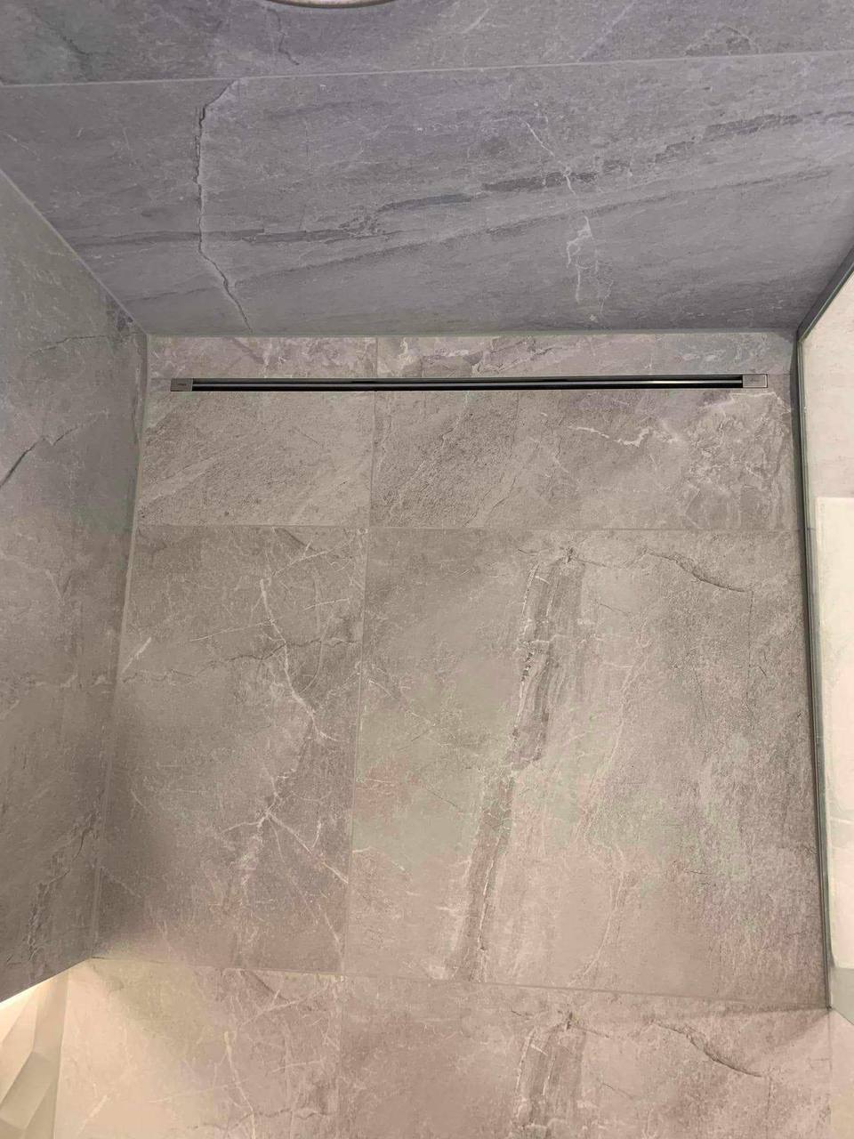 Szare płytki imitujące marmur w kabinie prysznicowej z odpływem liniowym. Minimalistyczny design, neutralna kolorystyka, nowoczesne wykończenie łazienki.