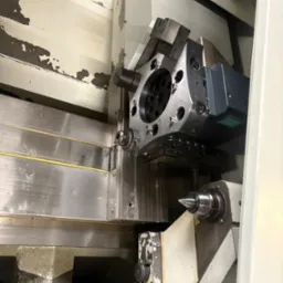 Wnętrze tokarki CNC z uchwytem narzędziowym i wrzecionem, widoczne ślady użytkowania na obudowie. Precyzyjna obróbka metali.