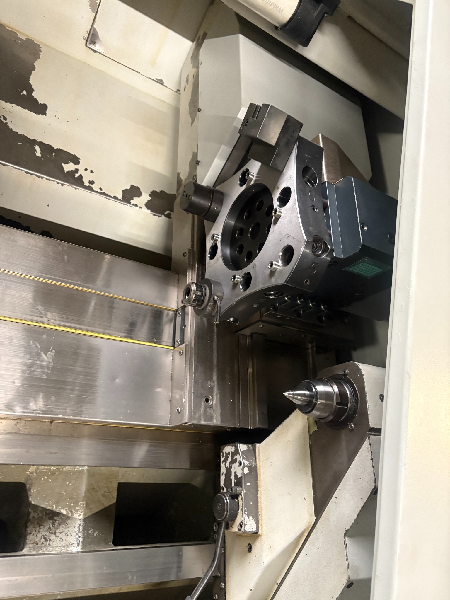 Wnętrze tokarki CNC z uchwytem narzędziowym i wrzecionem, widoczne ślady użytkowania na obudowie. Precyzyjna obróbka metali.