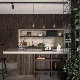 Nowoczesna kuchnia z ciemnego drewna, szary blat, oświetlenie punktowe i dekoracyjna roślina pnąca na metalowej konstrukcji. Minimalistyczny design z elementami naturalnymi.