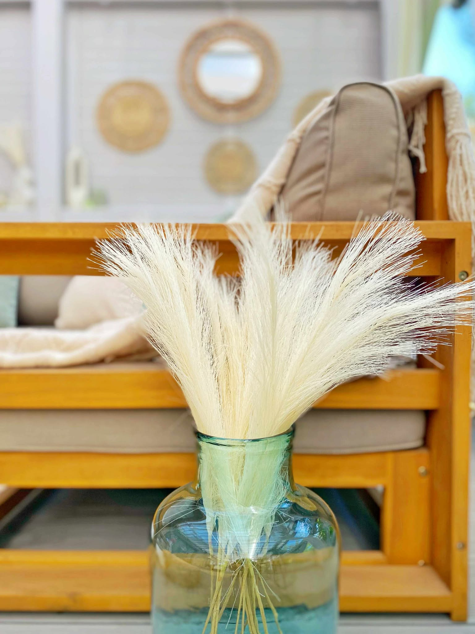 Jasny bukiet w turkusowym wazonie na tle drewnianego mebla i dekoracji ściennych w stylu boho. Detal aranżacji wnętrza, ciepłe światło.