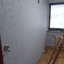 Arkadiusz Arko-Rem - Niebieska ściana z fakturą, przygotowana do prac wykończeniowych. Widoczna drabina, zabezpieczona folią okno i wystające kable ze ściany.