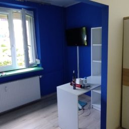 Arkadiusz Arko-Rem - Pokój po malowaniu: ściany w odcieniach niebieskiego i beżu, białe meble, widoczny kubeł z farbą. Ujęcie z perspektywy podłogi, podkreślające świeżość i kontrast kolorów.