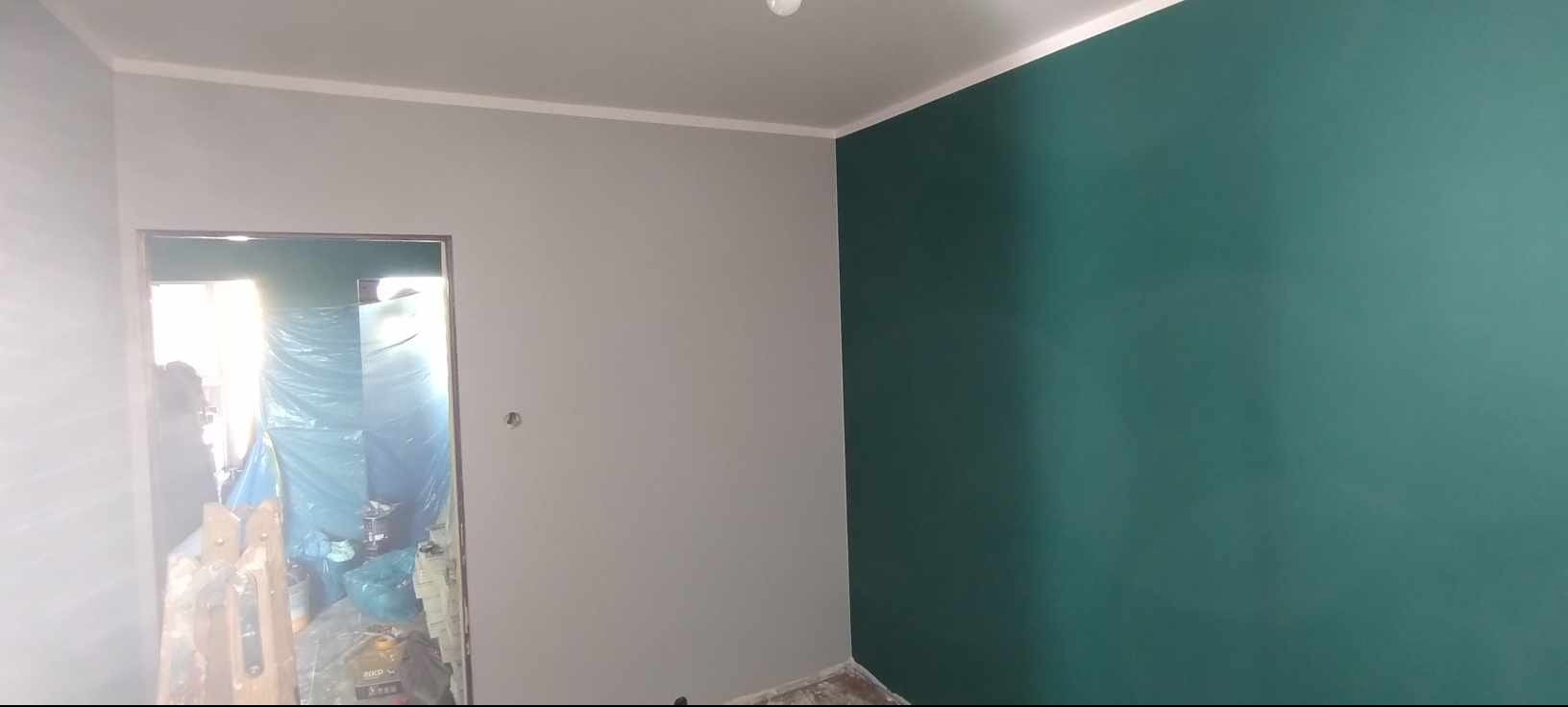 Pomieszczenie po malowaniu: szara ściana sąsiaduje z zieloną, widoczne zabezpieczenia w przejściu. Wykończenie wnętrza po odświeżeniu.