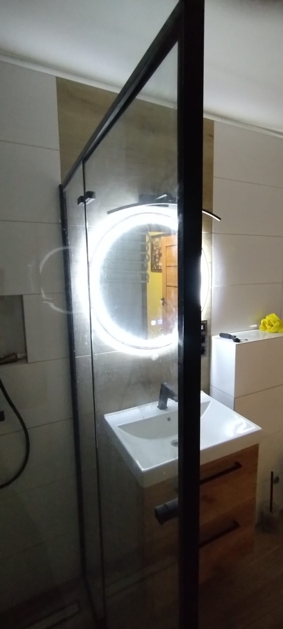 Nowoczesna łazienka z kabiną prysznicową typu walk-in, umywalką nablatową na szafce z drewnianymi frontami i okrągłym lustrem z podświetleniem LED.