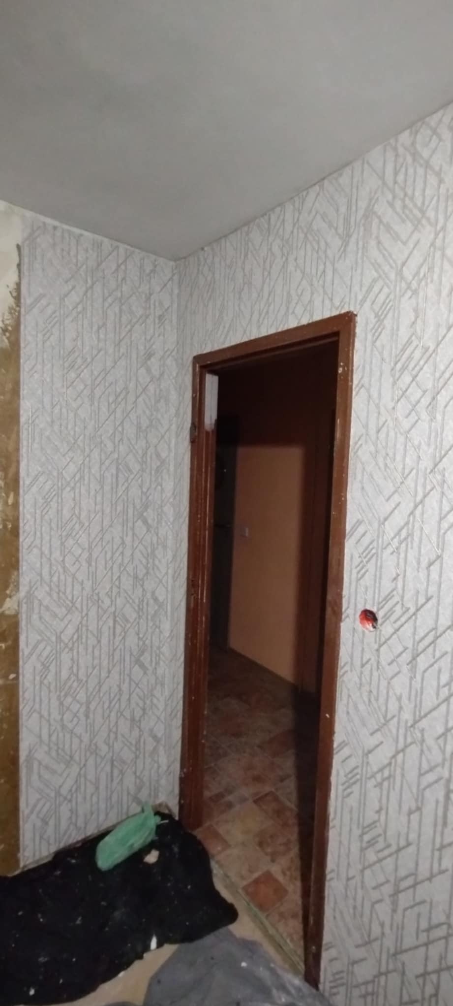 Pokój po tapetowaniu ścian z widoczną futryną drzwiową. Fragment ściany przed tapetowaniem. Podłoga zabezpieczona folią. Widoczne gniazdko elektryczne.