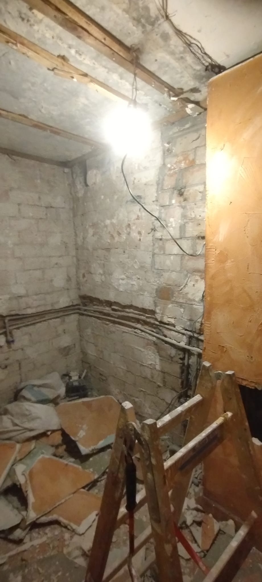 Pokój w trakcie demontażu: odsłonięta cegła, instalacje, resztki płytek, drabina malarska. Widoczne ślady wcześniejszych prac i przygotowanie do dalszych etapów remontu.