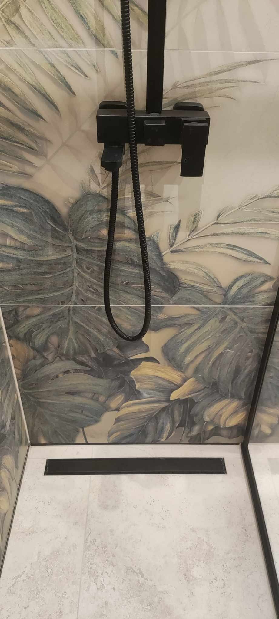 Nowoczesna kabina prysznicowa z czarną armaturą i odpływem liniowym, wykończona płytkami z motywem tropikalnych liści. Minimalistyczny design.