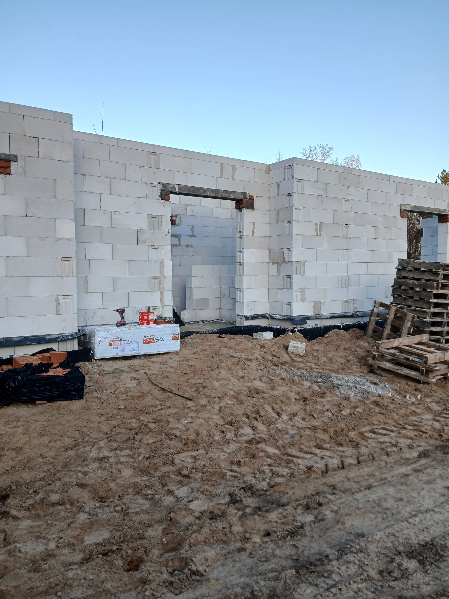 Wznoszone ściany domu z betonu komórkowego. Widoczne bloczki, zaprawa, narzędzia i materiały izolacyjne. Częściowo ukończona konstrukcja w surowym stanie.