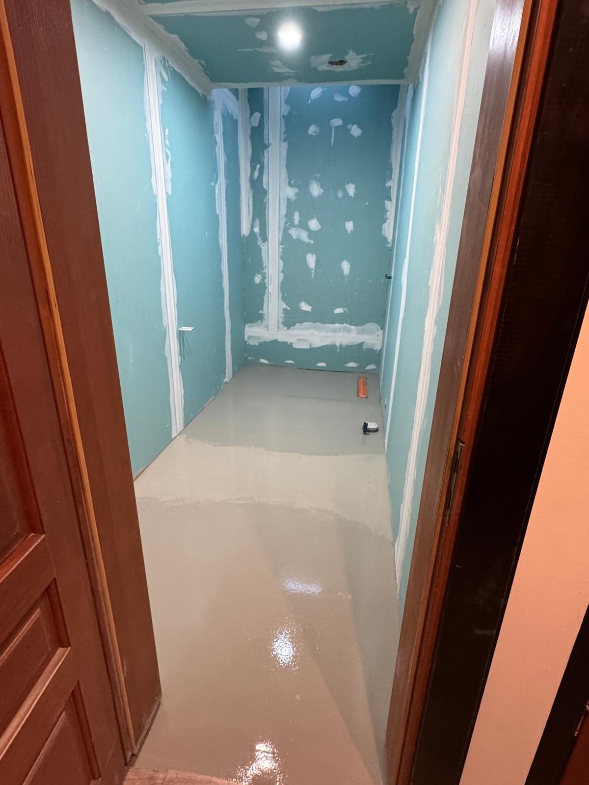 Wnętrze w trakcie prac wykończeniowych: wylewka podłogowa, ściany z płyt gipsowo-kartonowych z widocznymi łączeniami. Widok zza otwartych drzwi.